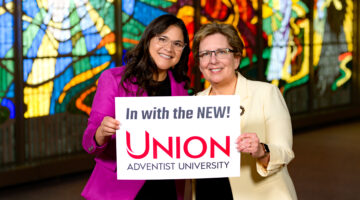 Photo of Dr. Bazan with Dr. Sauder holding a sign saying "In with the new! Union Adventist University"