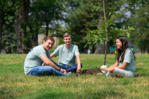 Photo of three students sitting under a sapling.